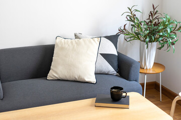 Wall Mural - Books and black cup of coffee on round wooden table in sofa background, cozy lifestyle concept. Scandinavian interior.