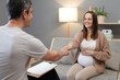 © sementsova321 - Cheerful brown haired Caucasian pregnant woman at therapy session handshaking with psychologist comes for therapy session sitting in cozy office on sofa meeting her counselor
