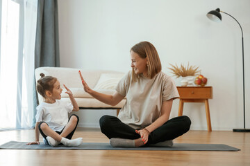 Sticker - Smiling, positive facial expression. Young woman with little girl are doing yoga at home