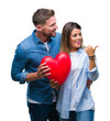 © Krakenimages.com - Young couple in love holding red heart over isolated background pointing and showing with thumb up to the side with happy face smiling