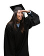 © Krakenimages.com - Young hispanic woman wearing graduated cap and uniform very happy and smiling looking far away with hand over head. Searching concept.
