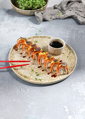 Canvas Print - Sliced Seared Philadelphia Roll with Spicy Sauce, Soy Sauce, and Red Chopsticks on Ceramic Plate in Rustic Setting