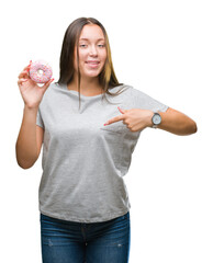 Young caucasian woman eating sweet donut over isolated background with surprise face pointing finger to himself