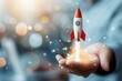 © pingpao - Hand holding a small rocket ship launching, symbolizing creativity, innovation, and startup success in a modern business environment.