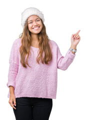 Wall Mural - Young beautiful brunette woman wearing sweater and winter hat over isolated background with a big smile on face, pointing with hand and finger to the side looking at the camera.