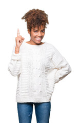 Wall Mural - Beautiful young african american woman wearing winter sweater over isolated background pointing finger up with successful idea. Exited and happy. Number one.