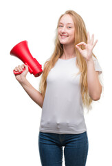 Wall Mural - Blonde teenager woman holding megaphone doing ok sign with fingers, excellent symbol