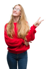 Poster - Blonde teenager woman wearing red sweater smiling with happy face winking at the camera doing victory sign. Number two.