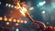 © Bundi - Concept of a hand holding a torch with the Olympic flame against the backdrop of a night stadium.