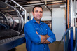 © Dasha Petrenko - A young smiling man in a denim shirt at the cheese factory. An attractive worker near a milk and a butter making machine. An engineer for the maintenance of a cheese production line.