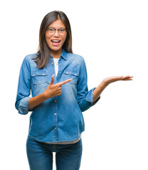 Wall Mural - Young asian woman wearing glasses over isolated background amazed and smiling to the camera while presenting with hand and pointing with finger.