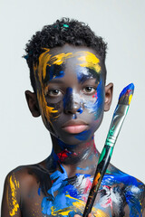 Sticker - A young boy with his face painted in bright colors holding a paintbrush.