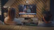 © Framestock - Adult couple watches news broadcast report about United States elections on big TV screen sitting on sofa. TV display shows playback of breaking news with female African American reporter. Back view.