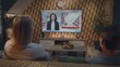 © Framestock - Back view of Caucasian couple watching breaking news about US presidential elections on big TV screen sitting on sofa at home. Television news broadcast with female news anchor displayed on TV display