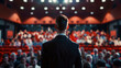 © Piyapat - A man giving a speech on stage with a large audience in a packed auditorium under bright lights.