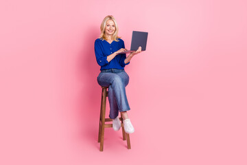 Sticker - Full body photo of attractive retired woman sit chair hold netbook dressed stylish blue clothes isolated on pink color background