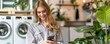 © jakapong - A woman sits in a bright laundry room using her phone, with washing machines in the background.