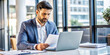 © hobonski - Focused Businessman Reviewing Documents at Office Desk. A serious businessman in a suit intently reviews documents while working on his laptop in a bright, modern office.