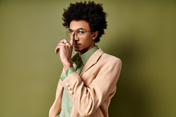 Stylish young African American man in trendy attire and glasses on a green background.