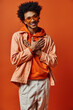 © LIGHTFIELD STUDIOS - A young African American man with curly hair wearing an orange jacket and sunglasses stands confidently against a bright orange background.