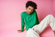 © LIGHTFIELD STUDIOS - young African American man with curly hair wearing casual green shirt and white pants on pink background.