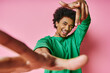 © LIGHTFIELD STUDIOS - A joyful African American man, curly hair in a green shirt, dances energetically on a vibrant pink background.
