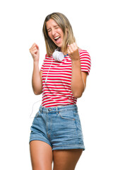 Poster - Young beautiful woman listening music wearing headphones over isolated background very happy and excited doing winner gesture with arms raised, smiling and screaming for success. Celebration concept.