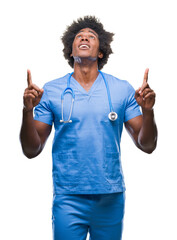 Sticker - Afro american surgeon doctor man over isolated background amazed and surprised looking up and pointing with fingers and raised arms.