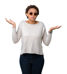 Wall Mural - Beautiful young african american woman wearing sunglasses over isolated background clueless and confused expression with arms and hands raised. Doubt concept.