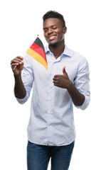 Wall Mural - Young african american man holding german flag happy with big smile doing ok sign, thumb up with fingers, excellent sign