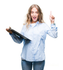 Canvas Print - Beautiful young blonde business woman holding clipboard over isolated background surprised with an idea or question pointing finger with happy face, number one