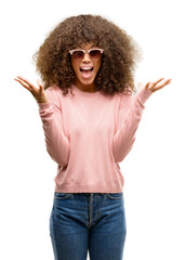 Wall Mural - African american woman wearing pink sunglasses celebrating crazy and amazed for success with arms raised and open eyes screaming excited. Winner concept