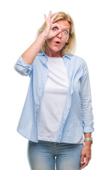 Poster - Middle age blonde woman over isolated background doing ok gesture shocked with surprised face, eye looking through fingers. Unbelieving expression.