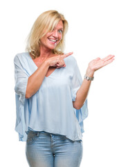 Wall Mural - Middle age blonde business woman over isolated background amazed and smiling to the camera while presenting with hand and pointing with finger.