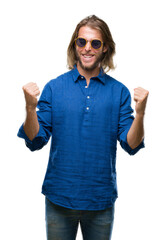 Poster - Young handsome man with long hair wearing sunglasses over isolated background very happy and excited doing winner gesture with arms raised, smiling and screaming for success. Celebration concept.