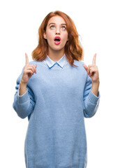 Canvas Print - Young beautiful woman over isolated background wearing winter sweater amazed and surprised looking up and pointing with fingers and raised arms.