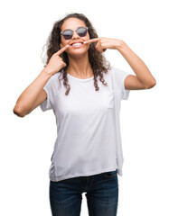 Poster - Young hispanic woman wearing sunglasses smiling confident showing and pointing with fingers teeth and mouth. Health concept.