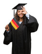 © Krakenimages.com - Young hispanic woman wearing graduation uniform holding flag of Germany with happy face smiling doing ok sign with hand on eye looking through fingers