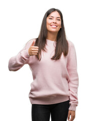 Sticker - Young beautiful hispanic woman wearing a sweater doing happy thumbs up gesture with hand. Approving expression looking at the camera with showing success.