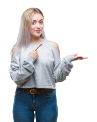 Sticker - Young blonde woman over isolated background amazed and smiling to the camera while presenting with hand and pointing with finger.