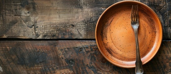 Leinwandbilder - Top view of a fork on an empty clay plate resting on a rustic wooden table with space for additional imagery