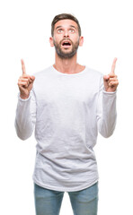 Wall Mural - Young handsome man over isolated background amazed and surprised looking up and pointing with fingers and raised arms.