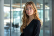 © sergign - Confident young woman standing in a modern, glass-walled office space, epitomizing professionalism and contemporary work environments.