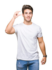 Wall Mural - Young handsome man wearing white t-shirt over isolated background smiling and confident gesturing with hand doing size sign with fingers while looking and the camera. Measure concept.