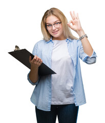 Poster - Young caucasian business woman holding clipboard over isolated background doing ok sign with fingers, excellent symbol