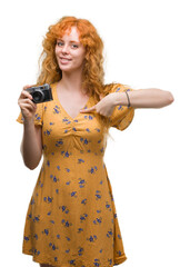 Poster - Young redhead woman taking pictures holding vintage camera with surprise face pointing finger to himself