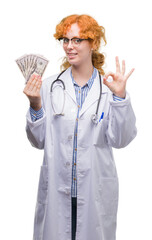 Poster - Young redhead doctor woman holding dollars doing ok sign with fingers, excellent symbol