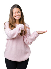 Wall Mural - Young beautiful brunette woman wearing pink winter sweater over isolated background amazed and smiling to the camera while presenting with hand and pointing with finger.