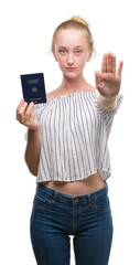 Poster - Blonde teenager woman holding passport of Germany with open hand doing stop sign with serious and confident expression, defense gesture