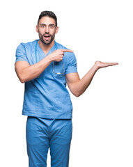 Poster - Handsome young doctor surgeon man over isolated background amazed and smiling to the camera while presenting with hand and pointing with finger.